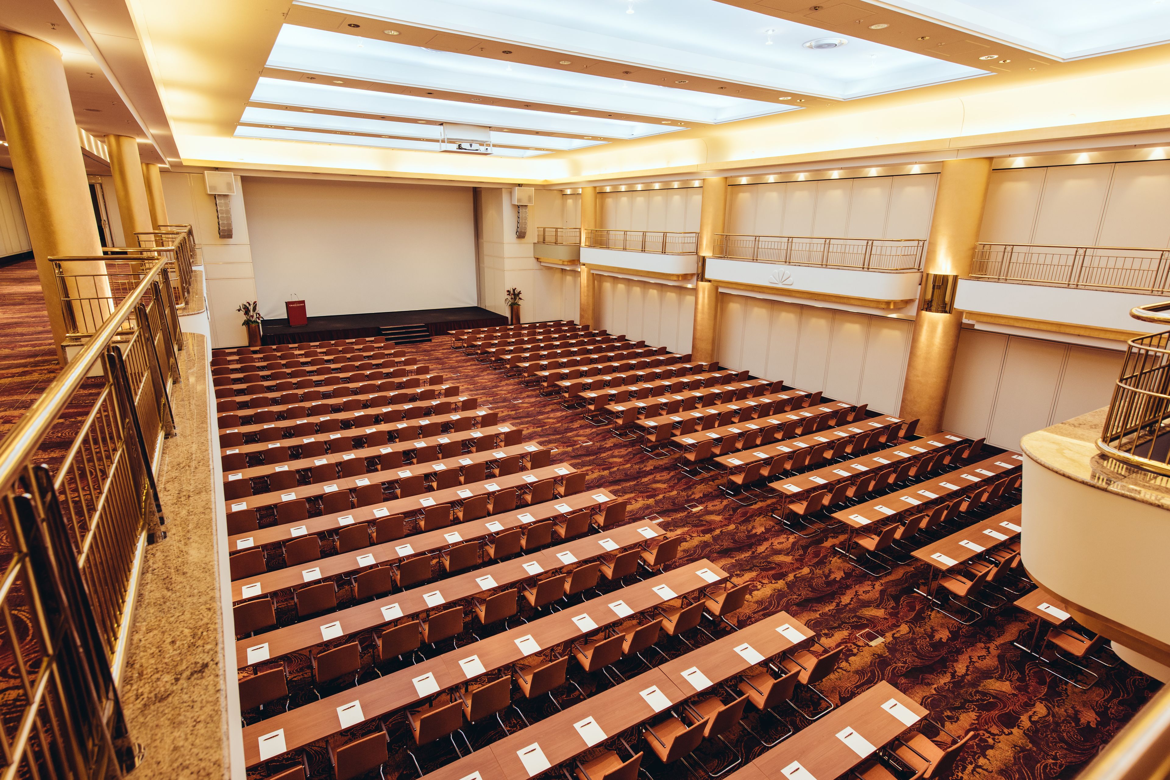 Ein großer Konferenzraum mit Tischen, Stühlen, einem Balkon und einem Oberlicht.