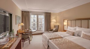 A hotel room with two beds, a desk with a chair, a television, and a window with curtains. - Grand Elysee Hamburg (Hamburg)