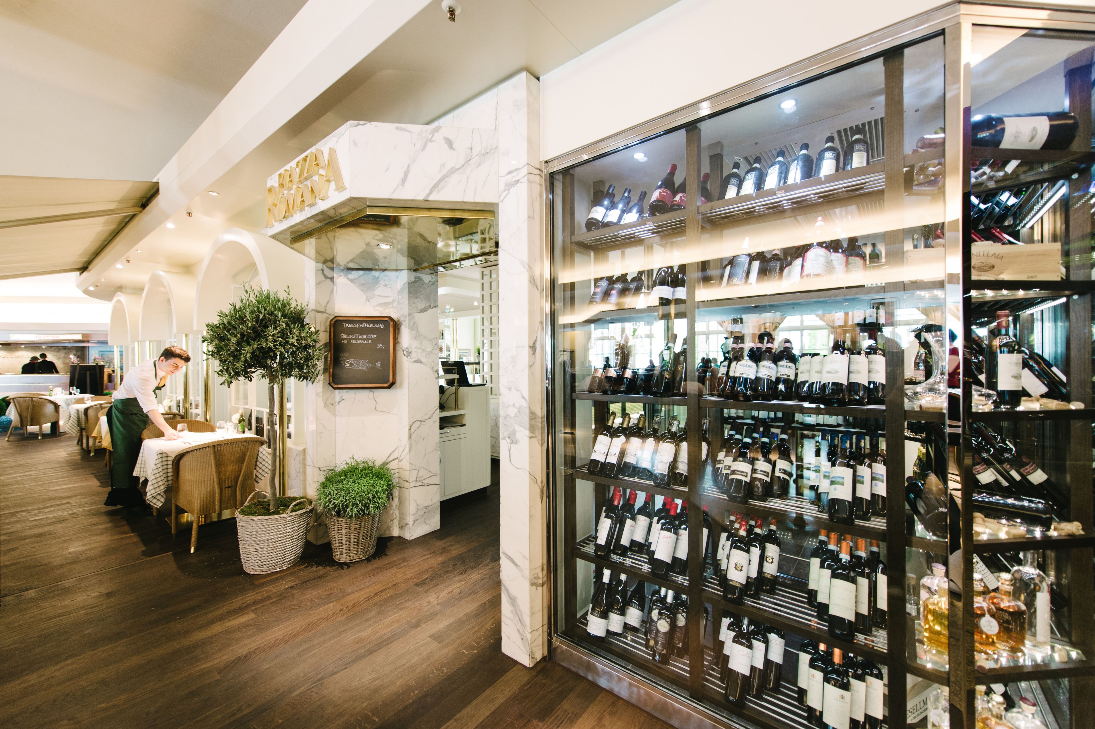Un restaurant où l’on peut admirer une collection de vins, et où un serveur s’occupe d’un client.