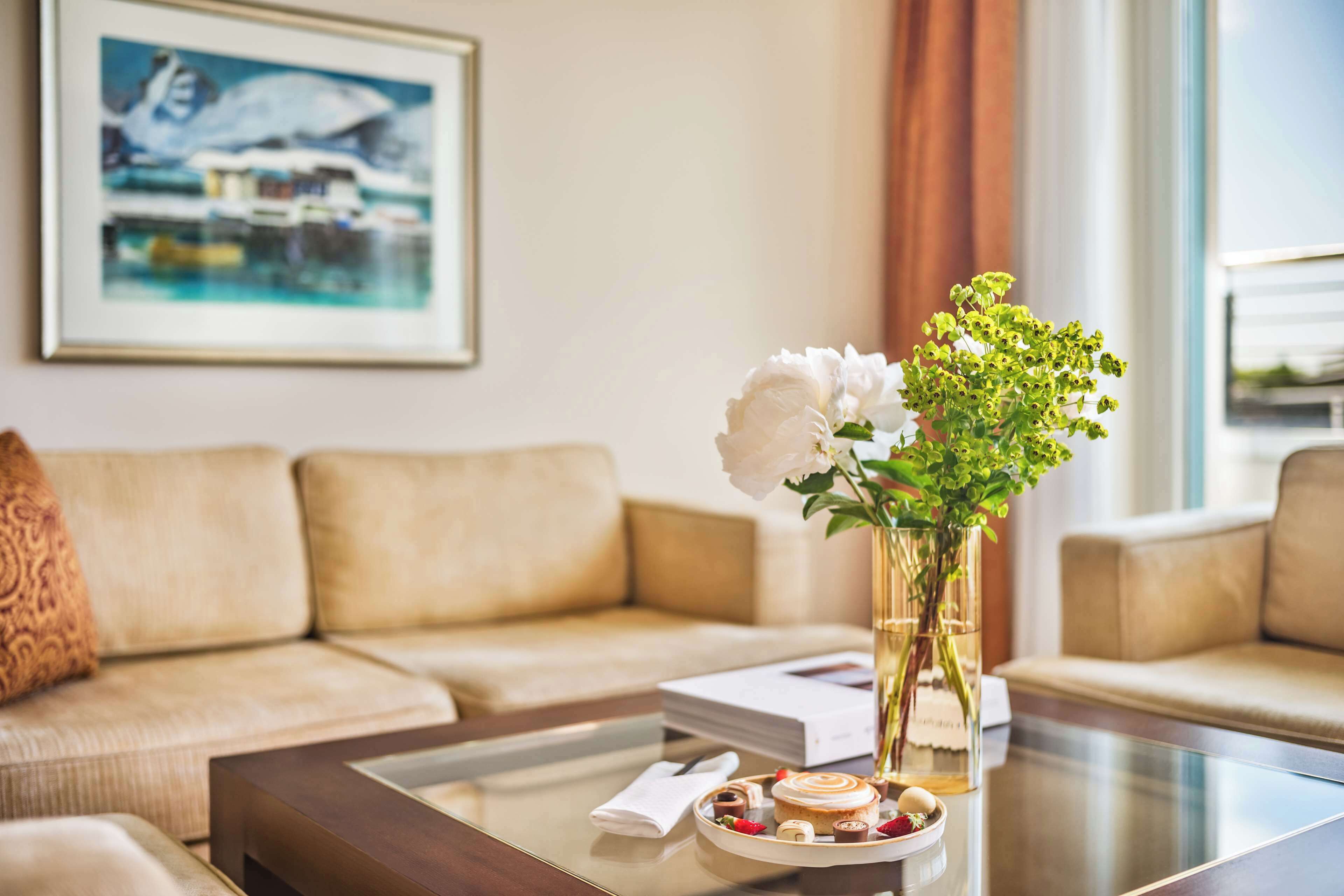 Una sala de estar con una mesa de centro de vidrio, un florero con flores y un libro.