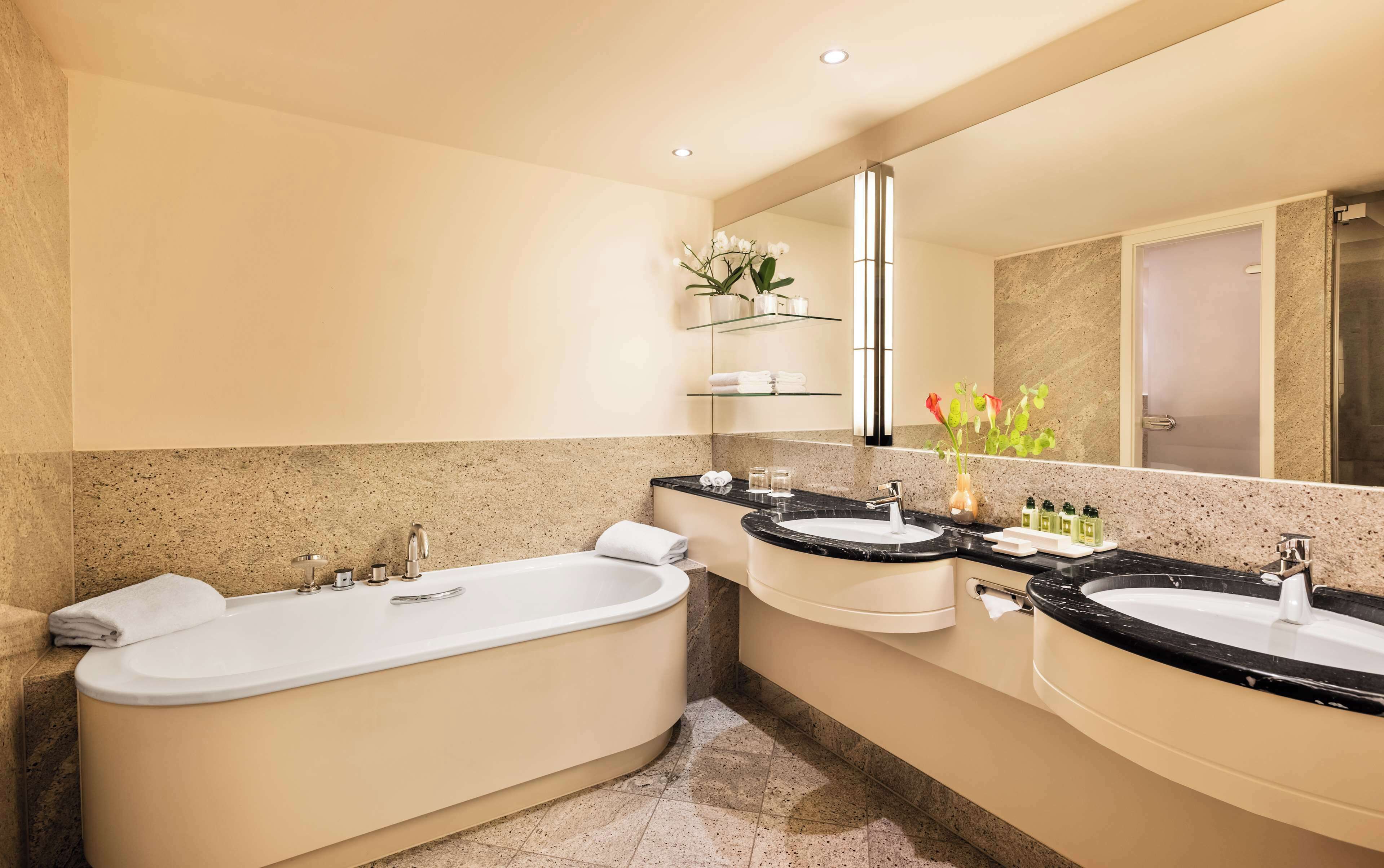 A modern bathroom with a freestanding bathtub, two sinks, and a large mirror.