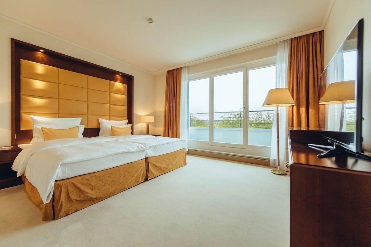 Habitación de hotel con una cama grande, dos mesitas de noche, un escritorio y un ventanal con cortinas.