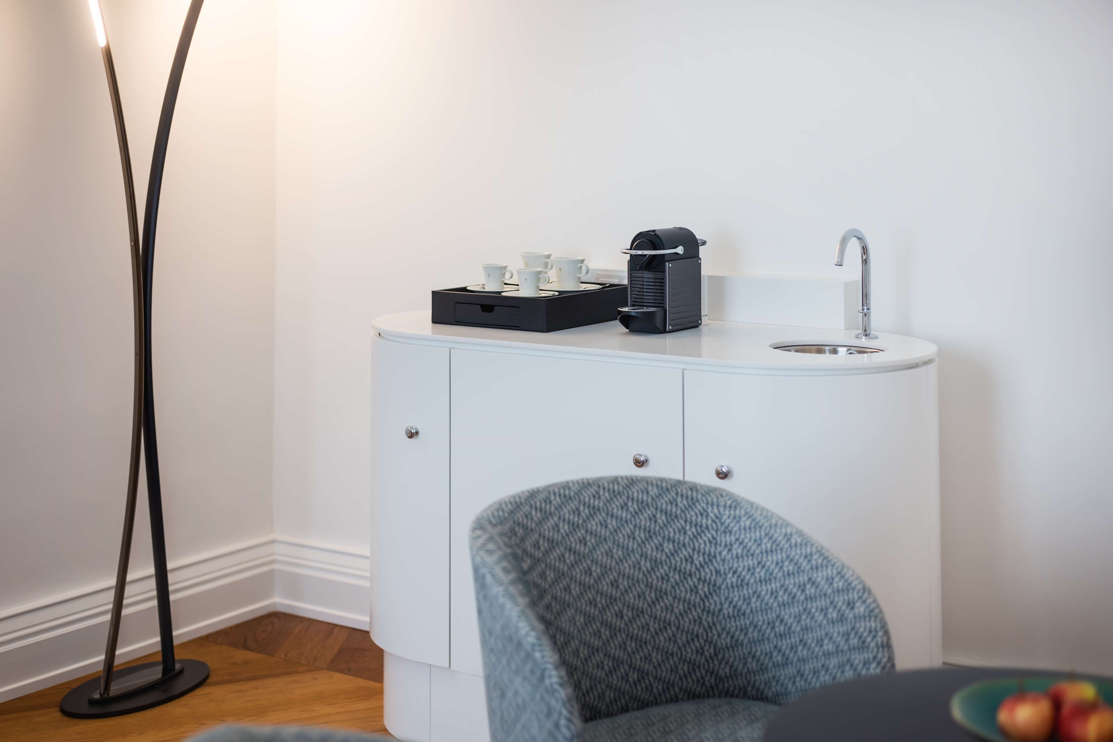 A compact kitchenette with a coffee maker, a sink, and a chair.