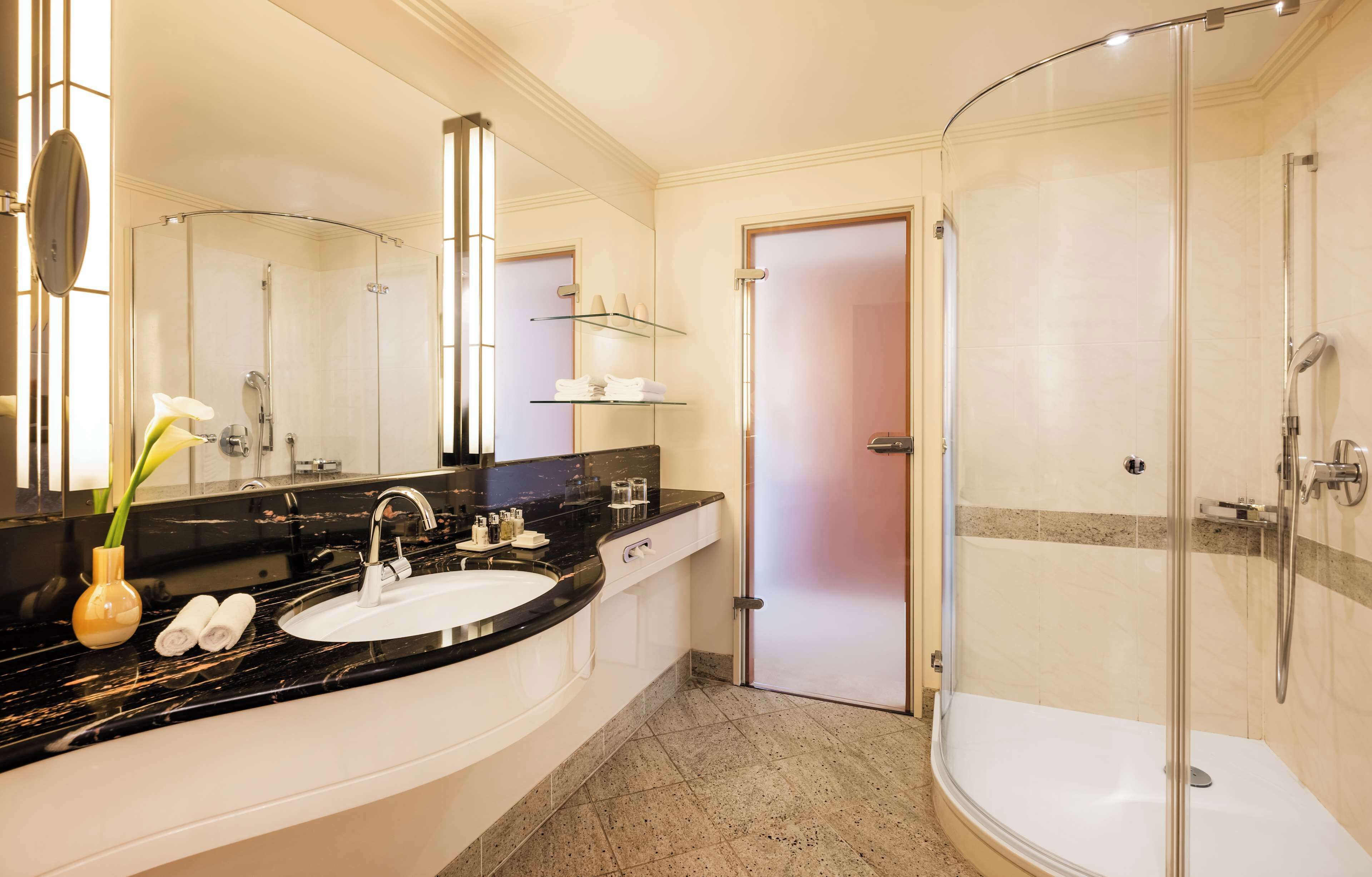 Un baño moderno con ducha curva, lavamanos blanco y un espejo grande.