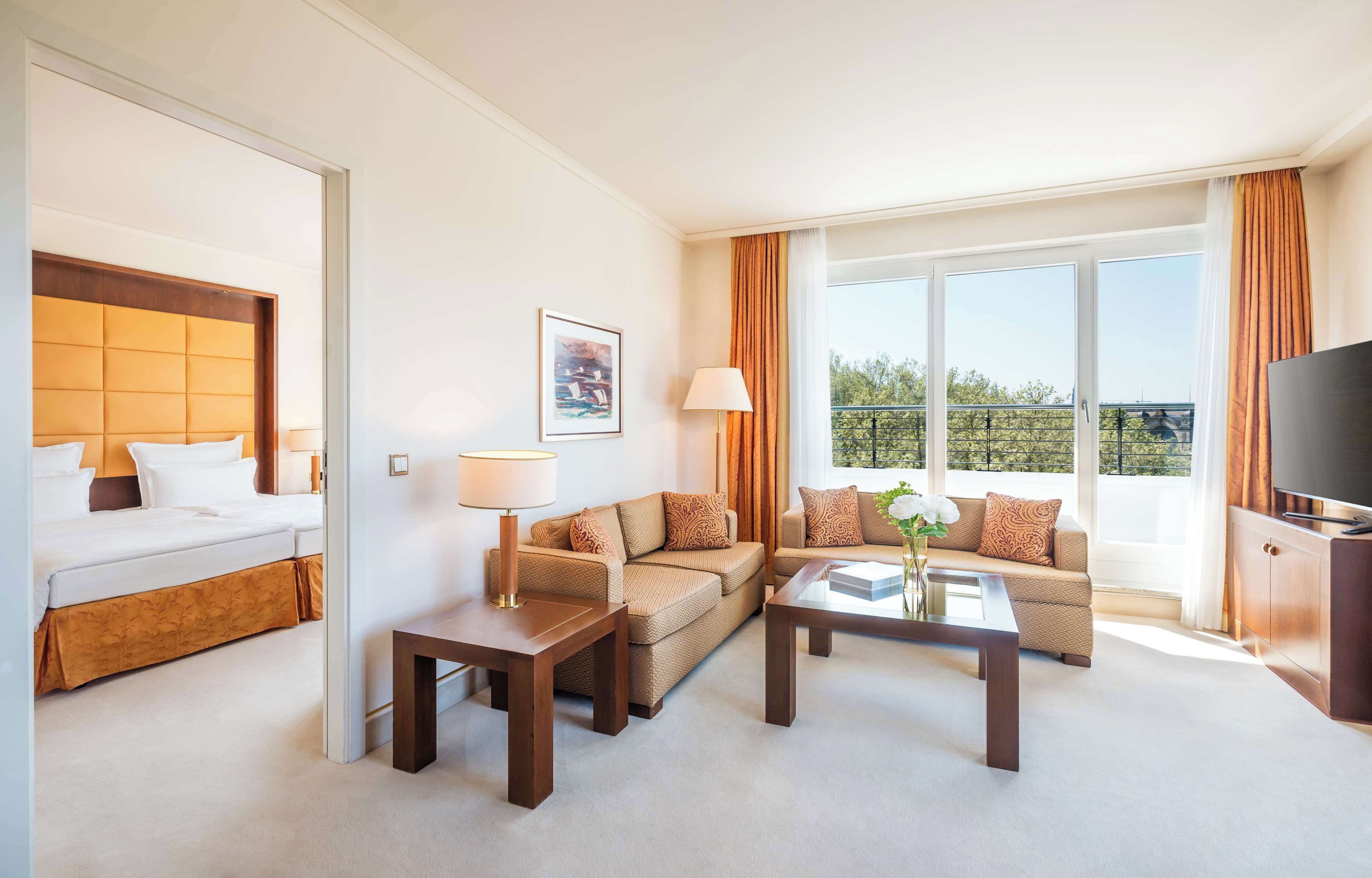 Habitación de hotel con cama, sofá, mesa de centro, televisor y balcón con vistas.