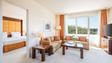 Habitación de hotel con cama, sofá, mesa de centro, televisor y balcón con vistas.