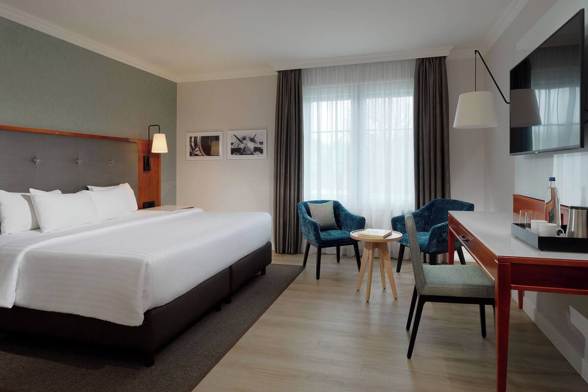 A hotel room with a large bed, a desk with a chair, a TV, and a window with curtains.