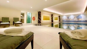 Habitación de hotel con dos camas mullidas verdes, un espejo grande, una pared con un mural de paisaje urbano y un separador de vidrio con un mosaico verde.