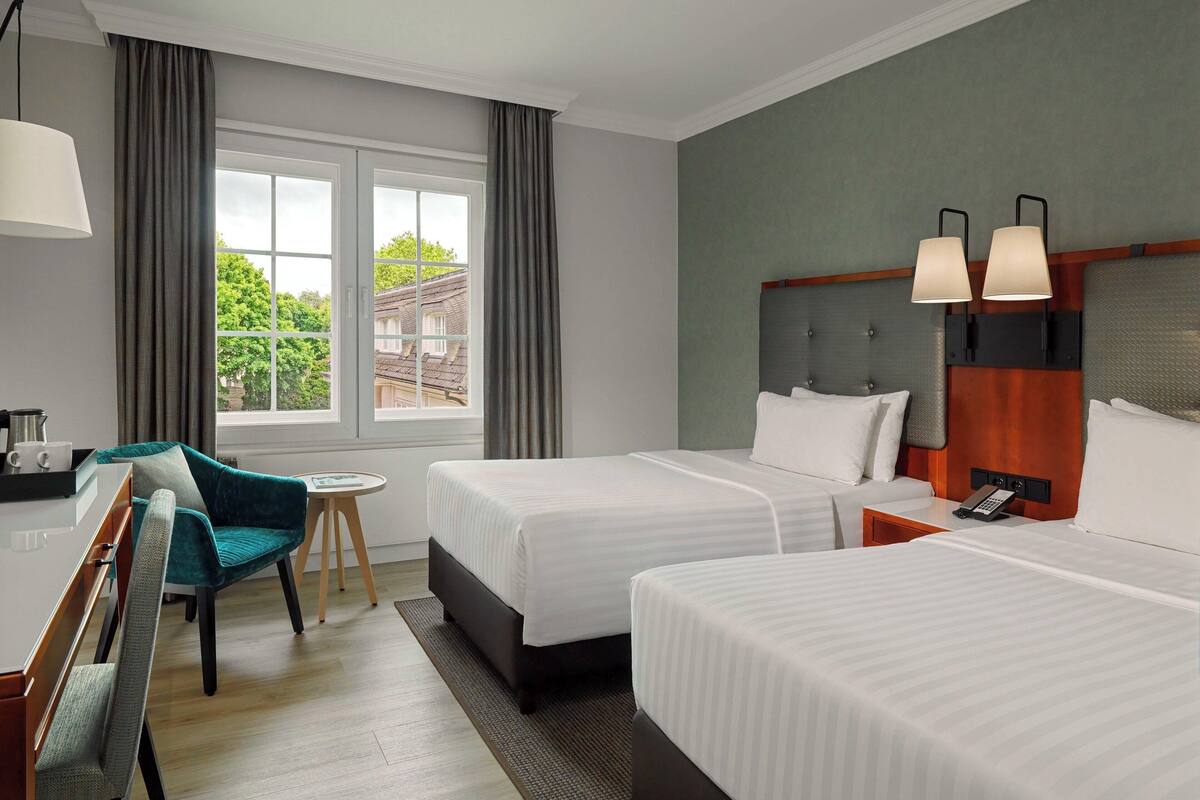 A hotel room with two beds, a desk, a chair, and a window with curtains.