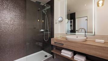 Un baño moderno con cabina de ducha de vidrio, tocador de madera y un espejo grande.