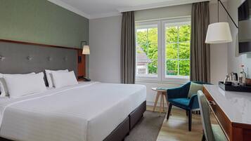 A hotel room with a large bed, a desk with a chair, a TV, and a window with curtains.