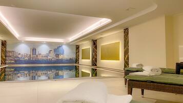 A hotel room with a cityscape mural, a bed with a green mattress, a small table with towels, and a wall-mounted light.