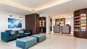 Un vestíbulo de hotel moderno con un conjunto de sofá azul, un cuadro abstracto grande y una zona de bar con botellas de vino.