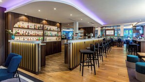 Un área de bar moderna con una barra curva, piso de madera y taburetes.