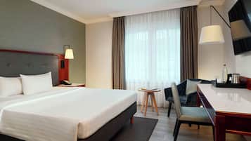 A hotel room with a large bed, a desk with a chair, a TV, and a window with curtains.