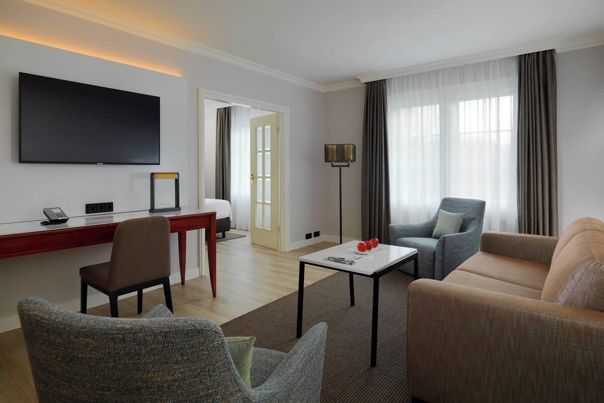 A modern hotel room with a flat-screen TV, a desk, a comfortable sofa, and a dining area.