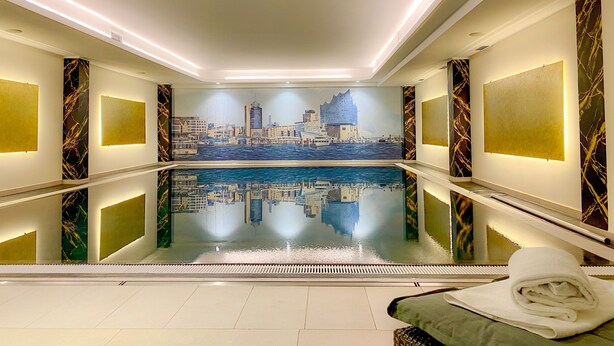 Una habitación de hotel moderna con un mural de paisaje urbano, un ventanal grande y una zona de piscina.