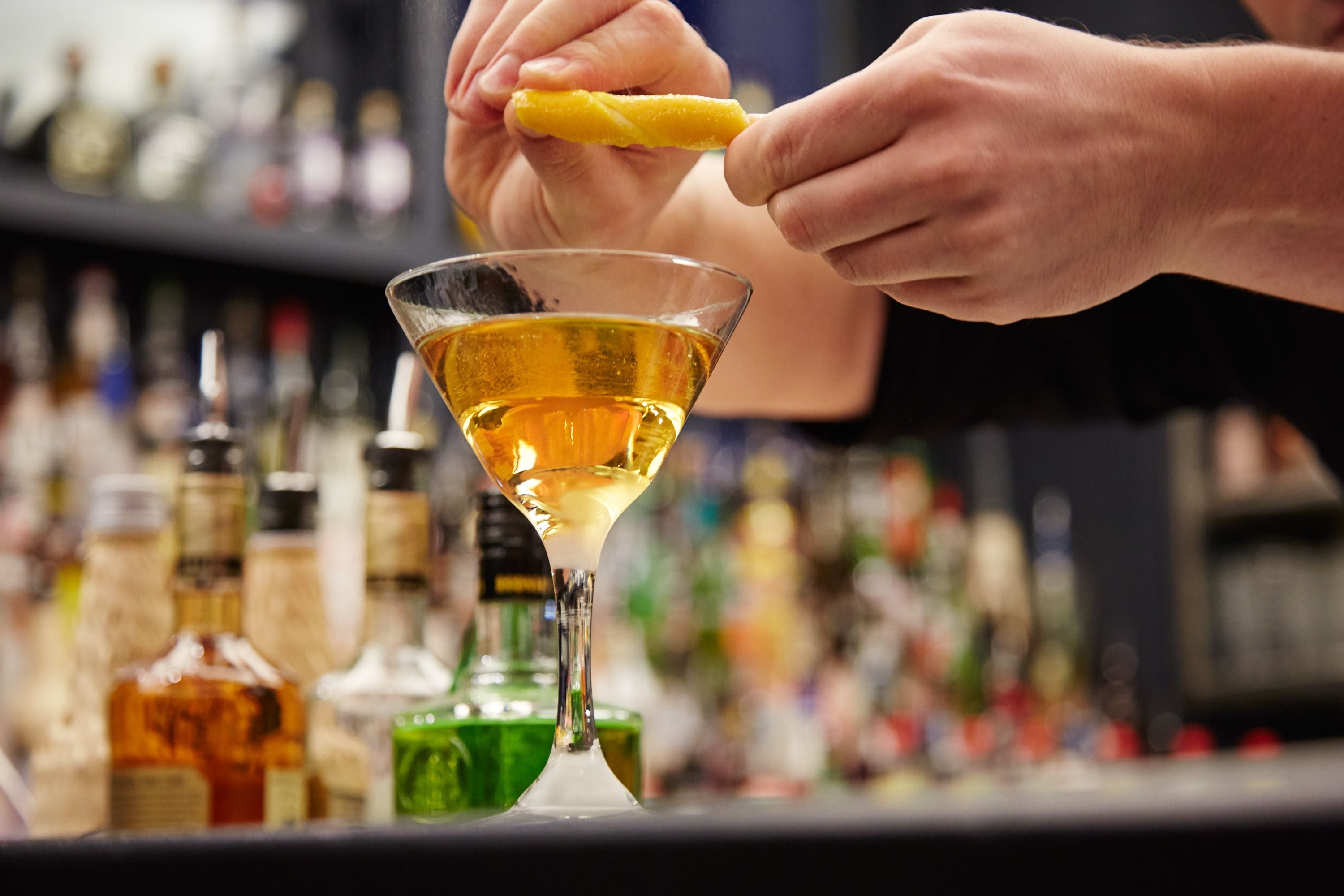 A bartender preparing a cocktail with a lemon twist.