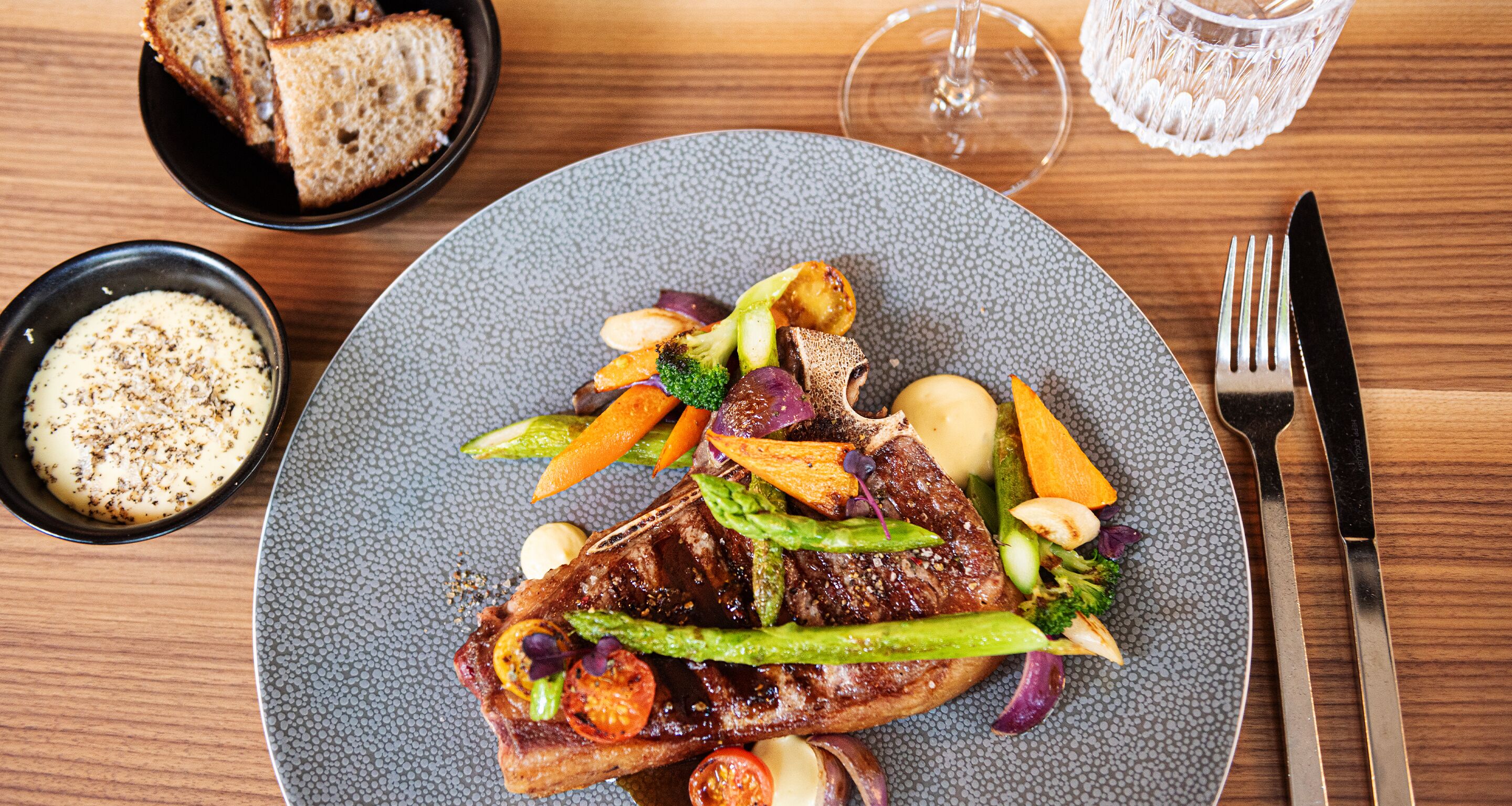 Un plato de comida con un bistec, verduras y un acompañamiento sobre una mesa.