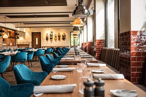 Ein Restaurant mit langen Holztischen, blauen Stühlen und hängenden Pendelleuchten.
