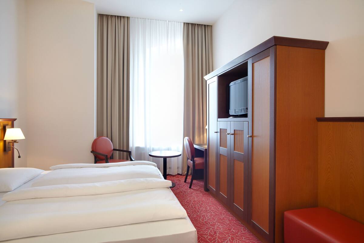 A hotel room with a large bed, a TV, a desk, and a chair.