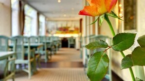 Une rose dans un couloir d’hôtel, avec des chaises et des tables vertes.