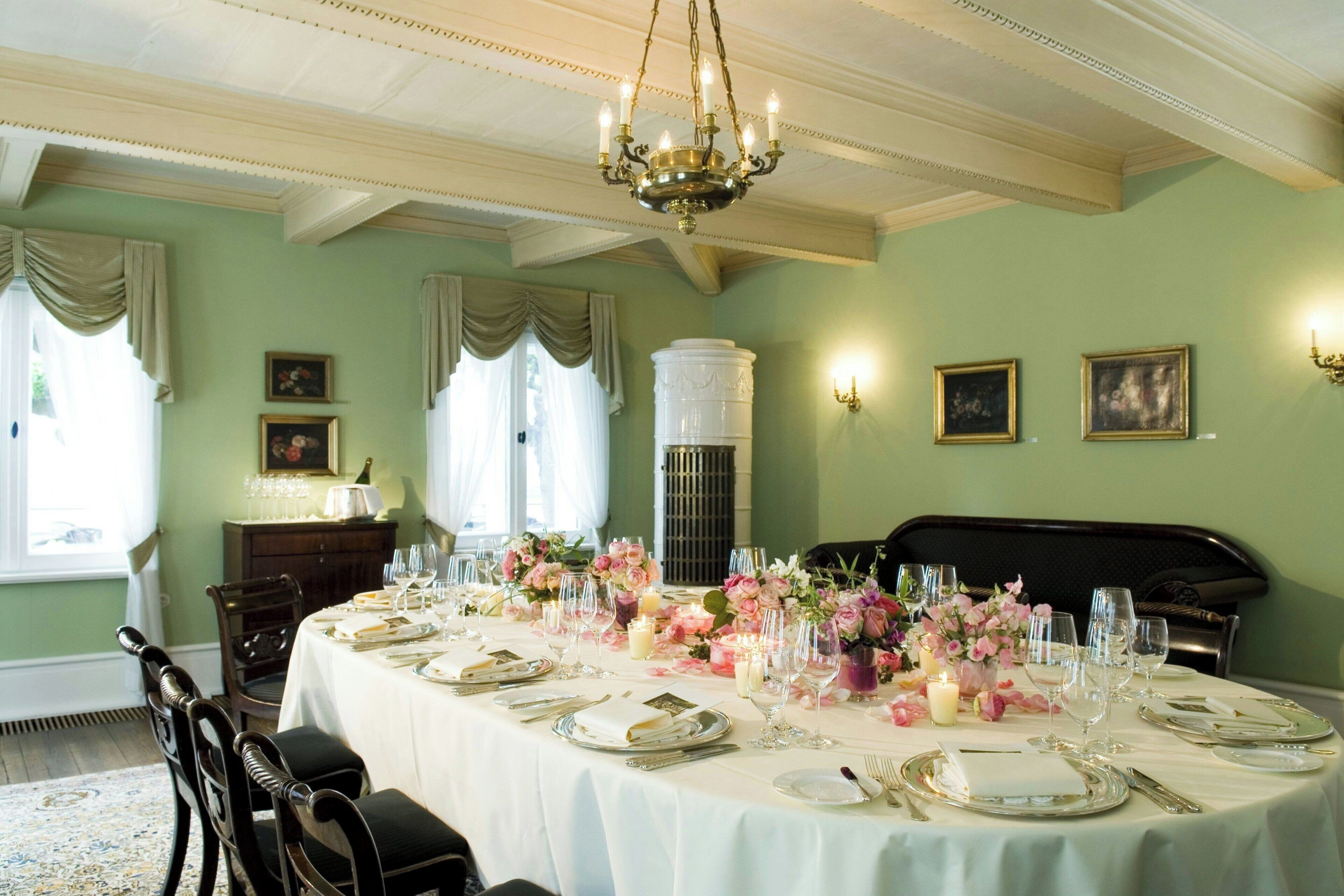 En formel spisesal med et rundt bord dækket til et måltid, elegante stole og en lysekrone.