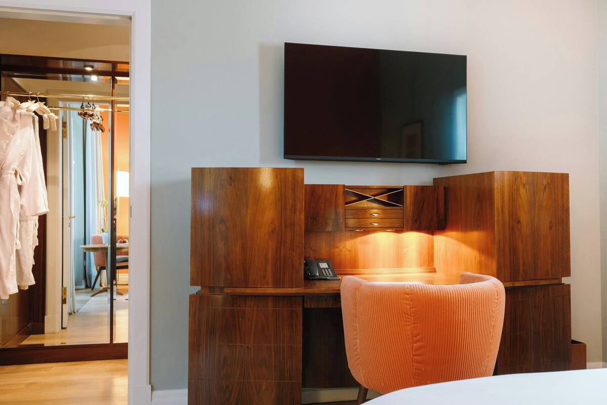 A hotel room with a wooden desk, a television mounted on the wall, and a mirror reflecting the room.