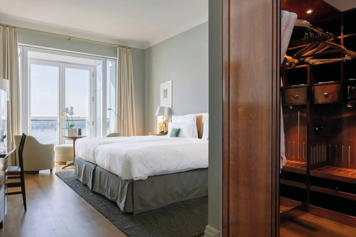 A hotel room with a large bed, a desk, a chair, a wardrobe, and a view of the outdoors.