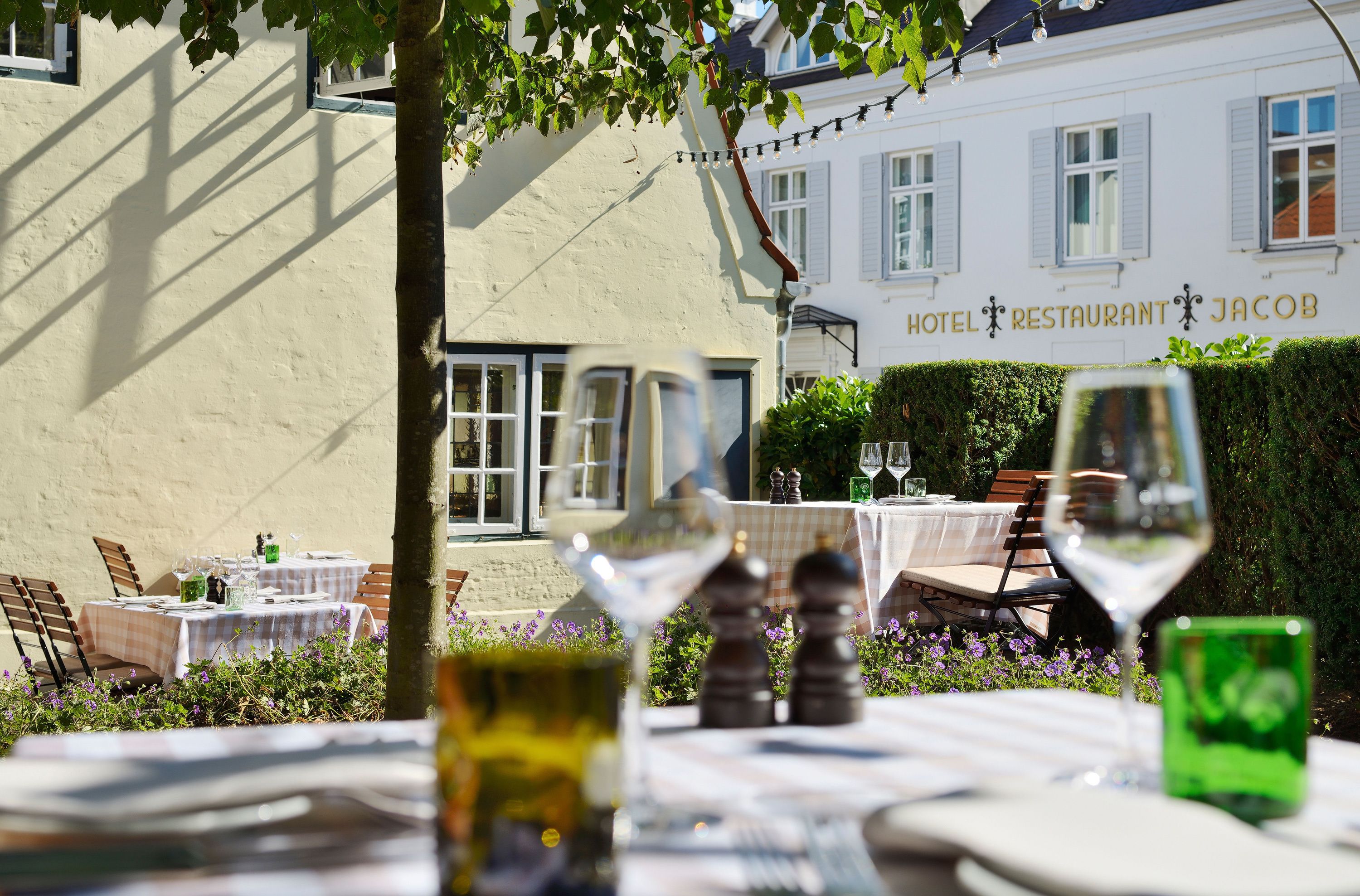An outdoor dining area with tables set for two, featuring wine glasses and salt shakers.
