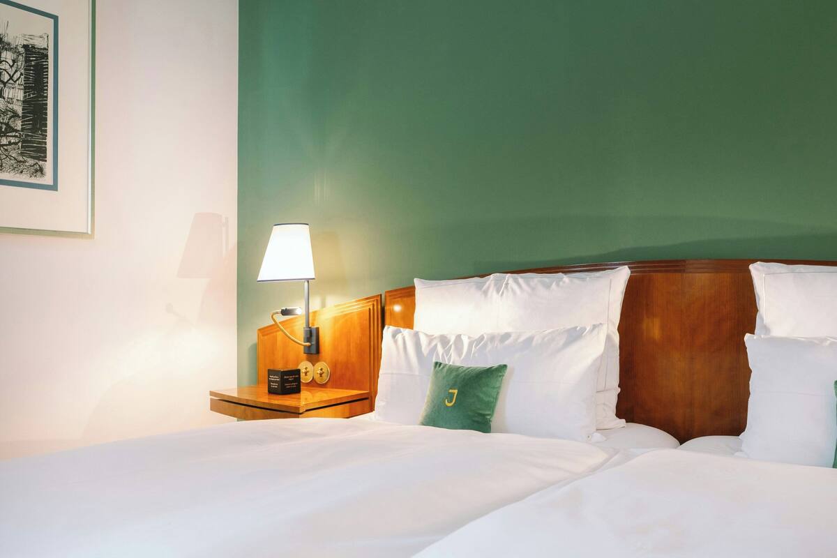 A hotel room with a large bed, a wooden headboard, a nightstand with a lamp, and a framed picture on the wall.