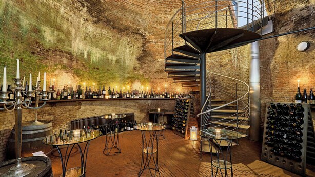 A wine cellar with a spiral staircase, wine racks, and a bar area. - Louis C. Jacob, Hamburg, Autograph Collection (Hamburg)