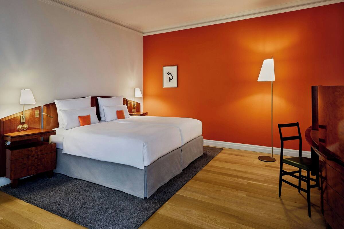 A hotel room with a bed, nightstands, a desk, a chair, and a floor lamp.