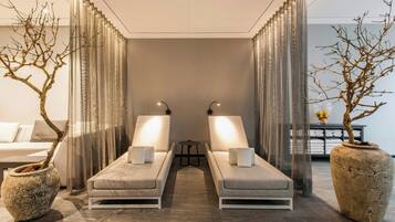 A spa room with two lounge chairs, a small table, and two large potted trees.
