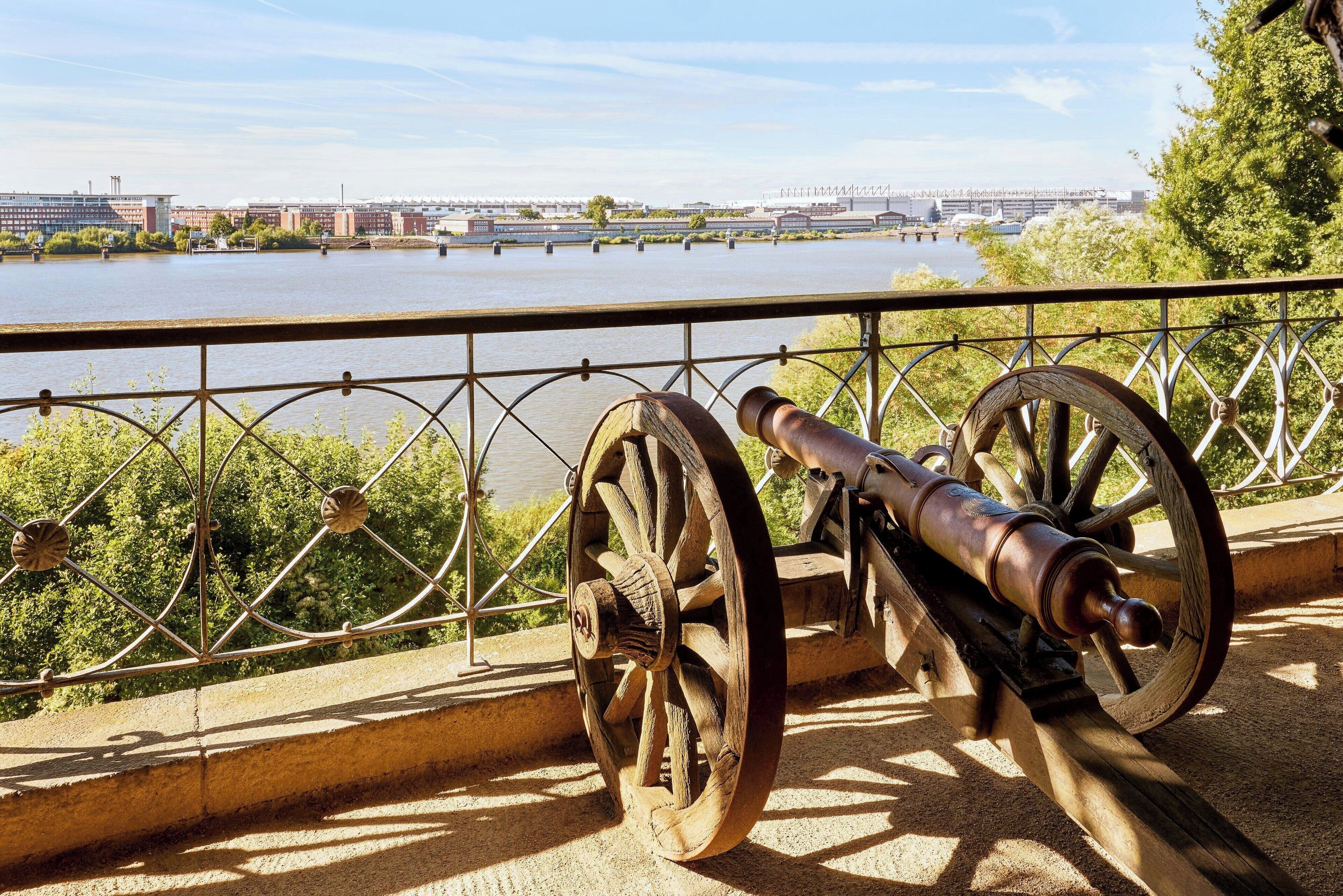 A cannon on a bridge overlooking a river with buildings in the background.