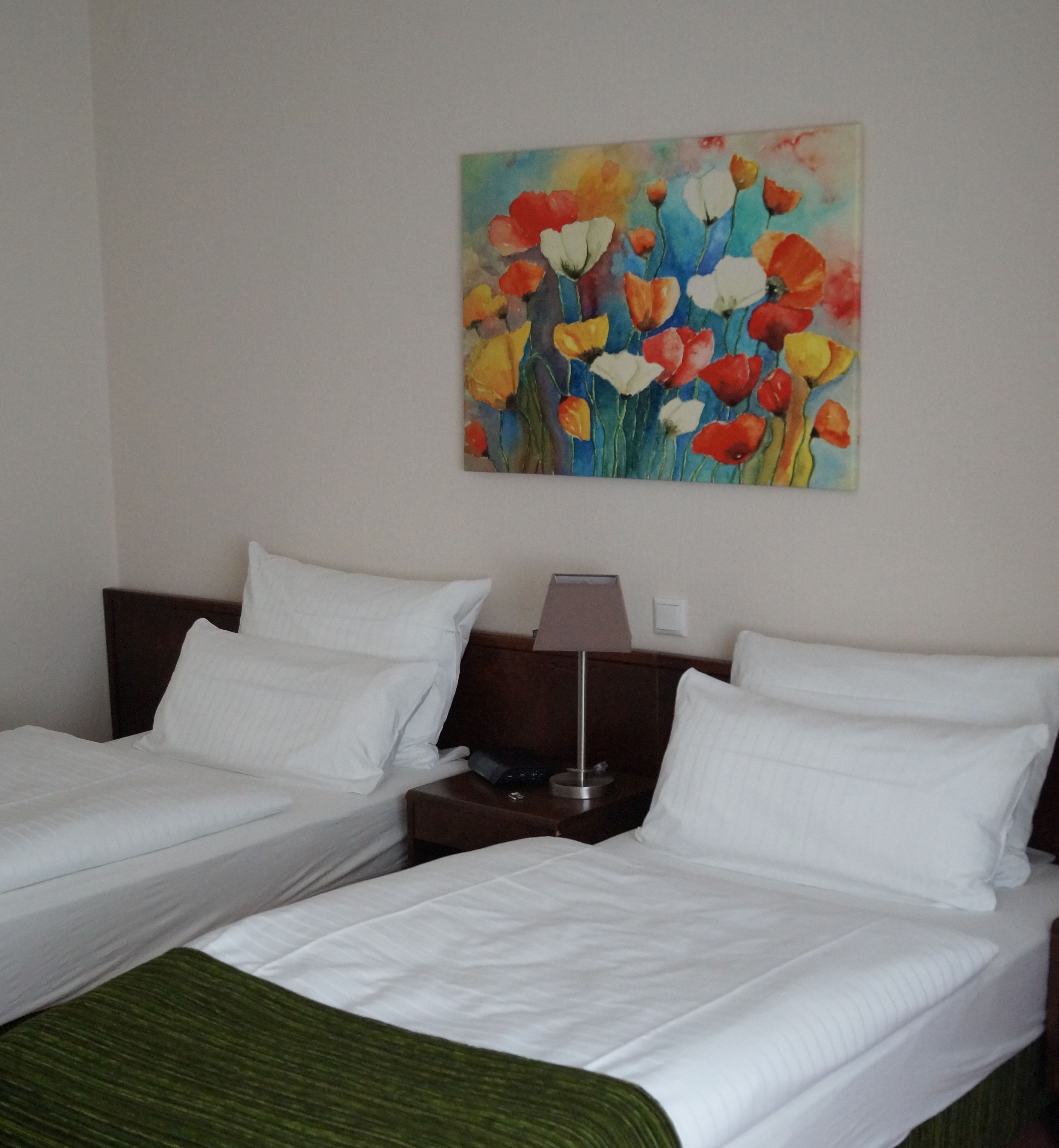 Habitación de hotel con dos camas, una mesita de noche, una lámpara y un cuadro de flores en la pared.