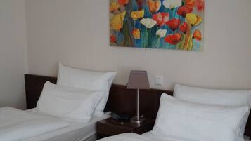 Habitación de hotel con dos camas, una mesita de noche, una lámpara y un cuadro de flores en la pared.