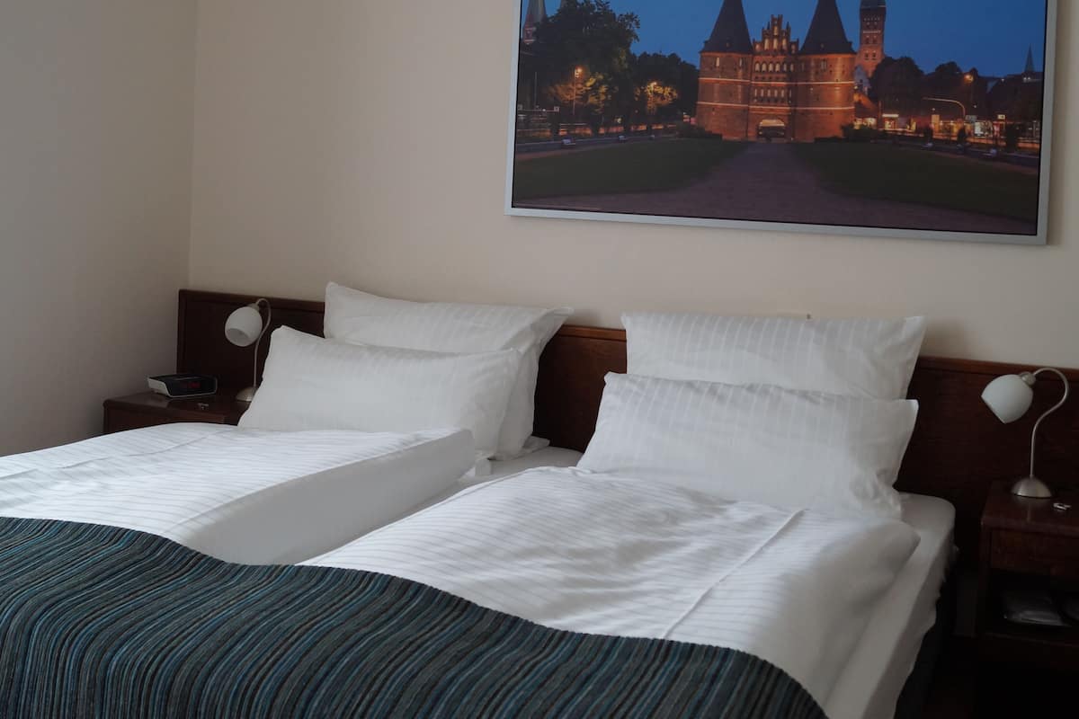 A hotel room with two beds, a large framed picture of a castle, and a nightstand with a lamp.