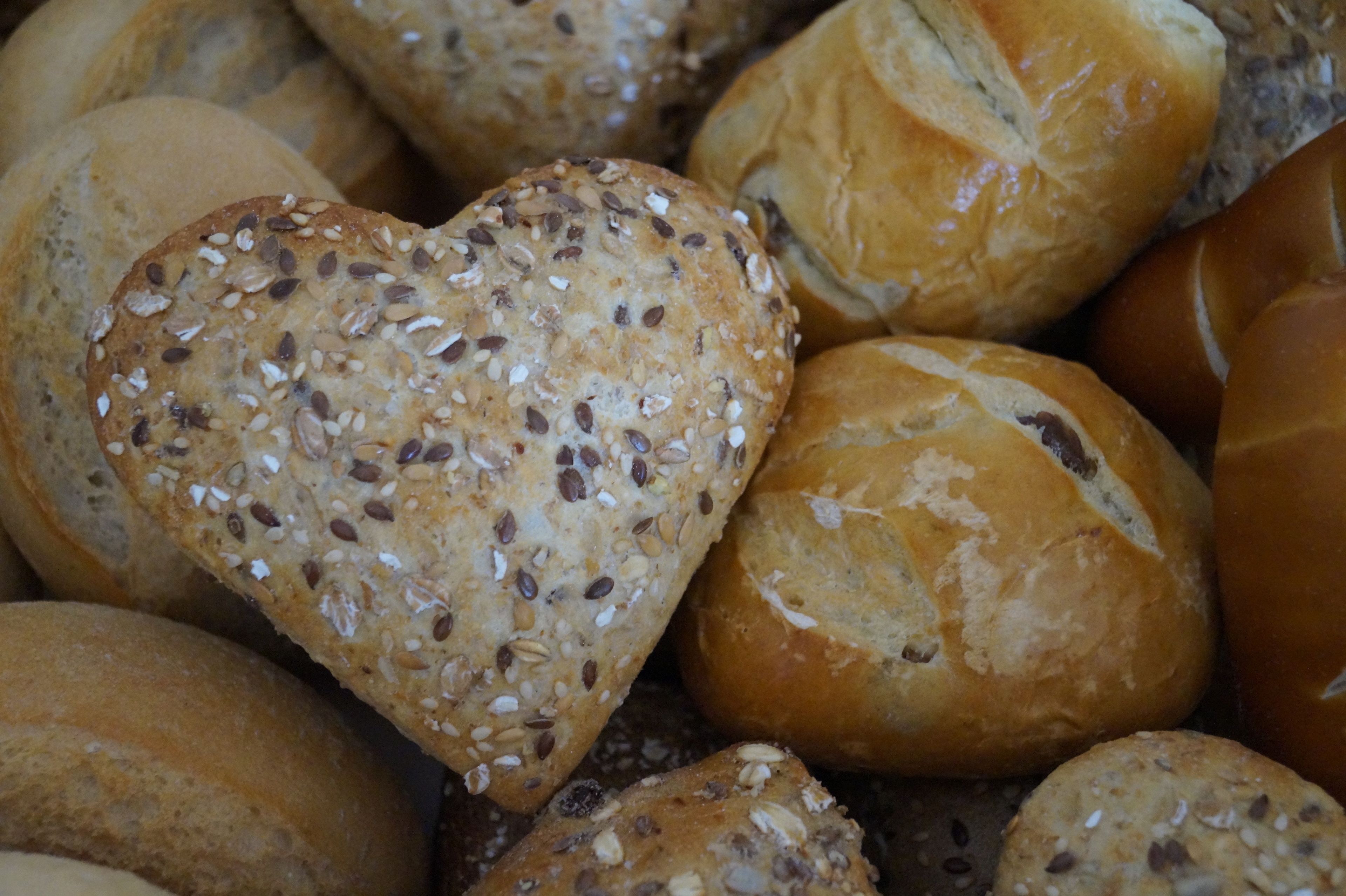 A variety of bread rolls, including a heart-shaped roll with seeds.