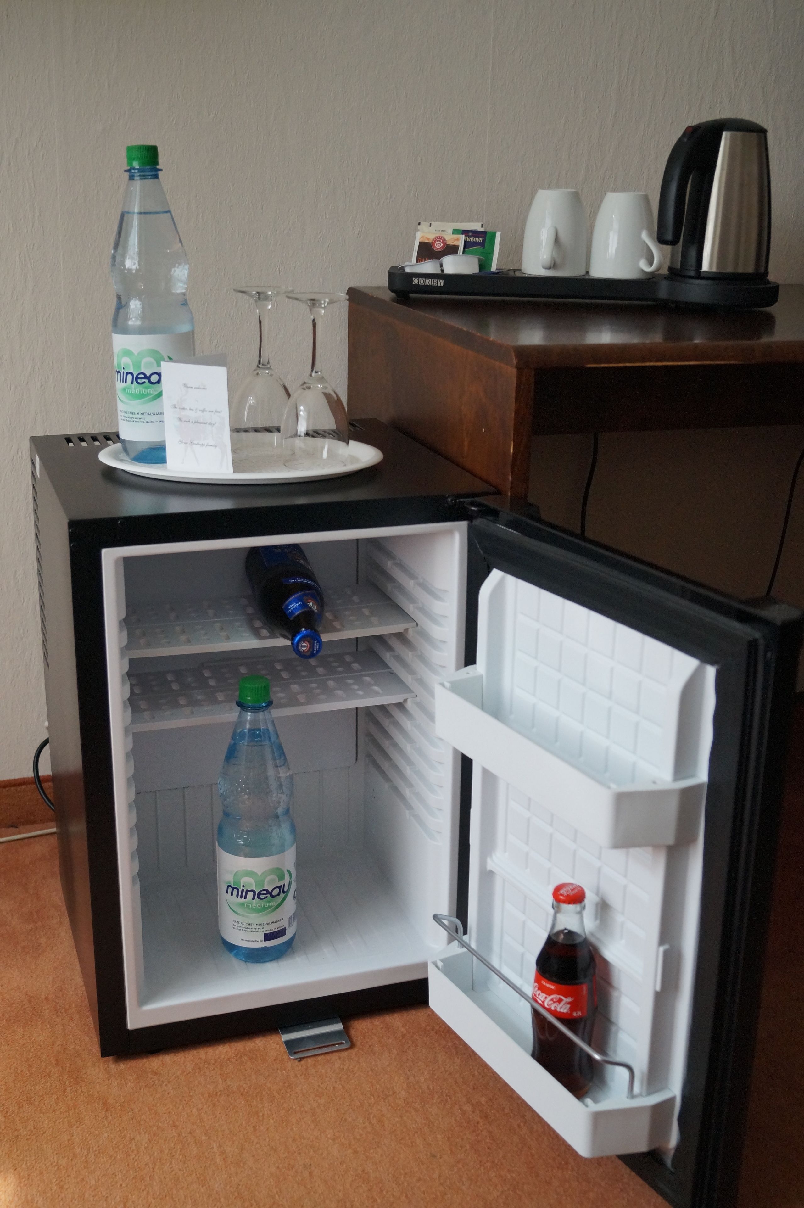 Ein kleiner Kühlschrank mit einem Weinglasständer, einer Wasserflasche und einer Colaflasche.