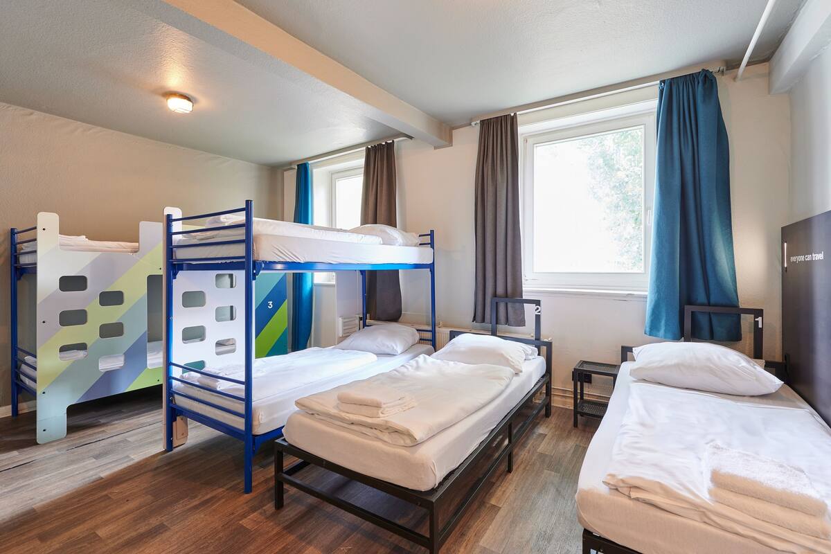 A room with bunk beds, a small table, and a window with curtains.