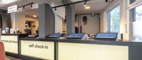 A self-check-in counter with digital kiosks, a reception area, and a window with natural light.