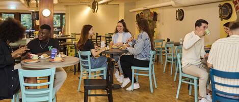 Un grupo de personas cenando en un restaurante con mesas y sillas redondas, pisos de madera y un ambiente relajado.