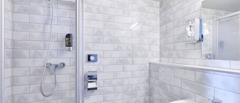 A modern bathroom with white tiled walls, a glass shower enclosure, a white toilet, and a sink with a mirror above it.