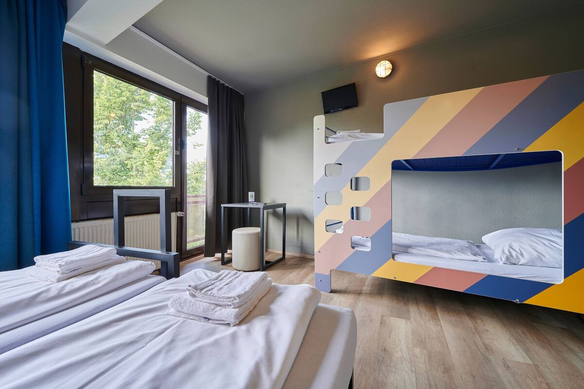 A hotel room with two beds, a television, and a window with curtains.