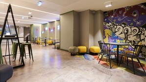 A modern interior with a colorful mural, a staircase, and a seating area with stools and tables.