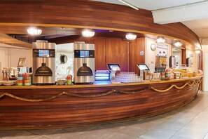 A wooden reception desk with a coffee machine, a digital screen, and a cash register.