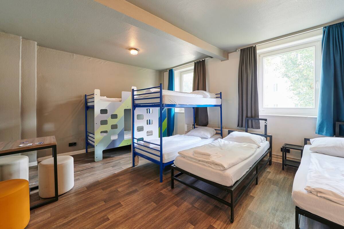 A dormitory room with bunk beds, a desk, and a window with curtains.