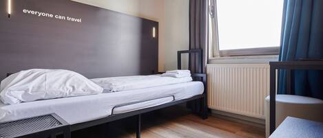 Een kleine, moderne hotelkamer met een enkel bed, een bureau en een raam met gordijnen.