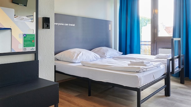 A hotel room with a bed, a desk, a television, and a window with curtains.